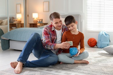 Photo of Father and son putting pocket money into piggybank at home