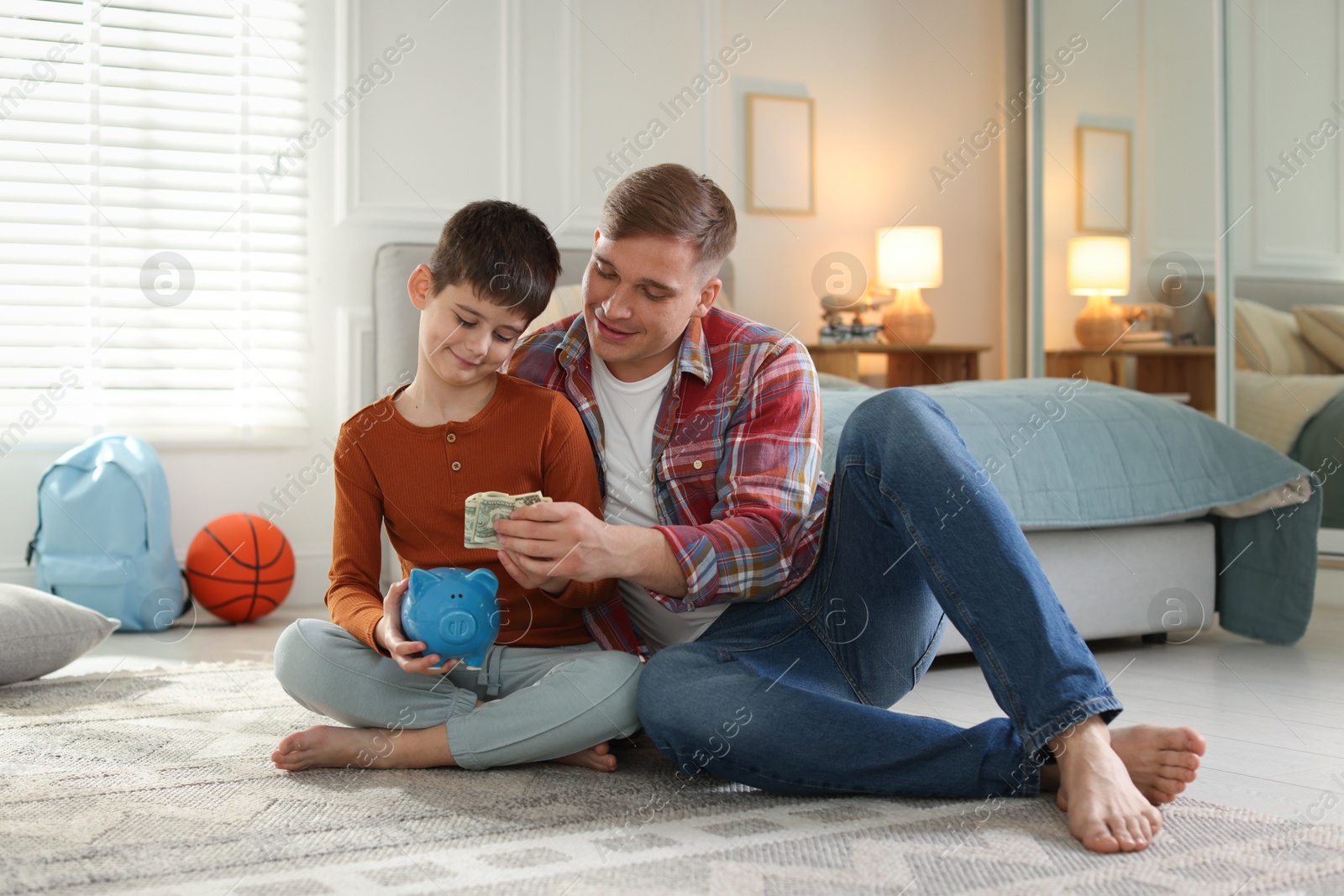 Father and son putting pocket money into piggybank at home Photo of Father and son putting pocket money into piggybank at home