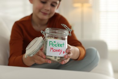 Photo of Boy with jar of pocket money on sofa at home, selective focus