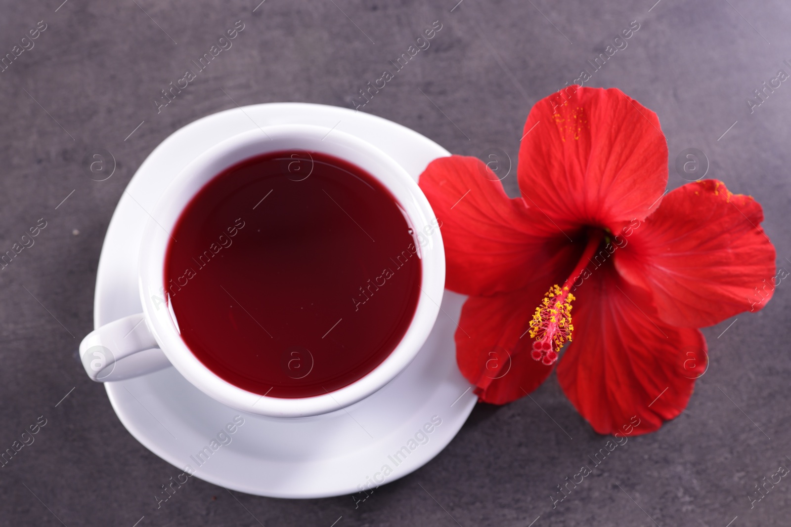 Tasty hibiscus tea in cup and beautiful flower on grey textured table, above view Photo of Tasty hibiscus tea in cup and beautiful flower on grey textured table, above view