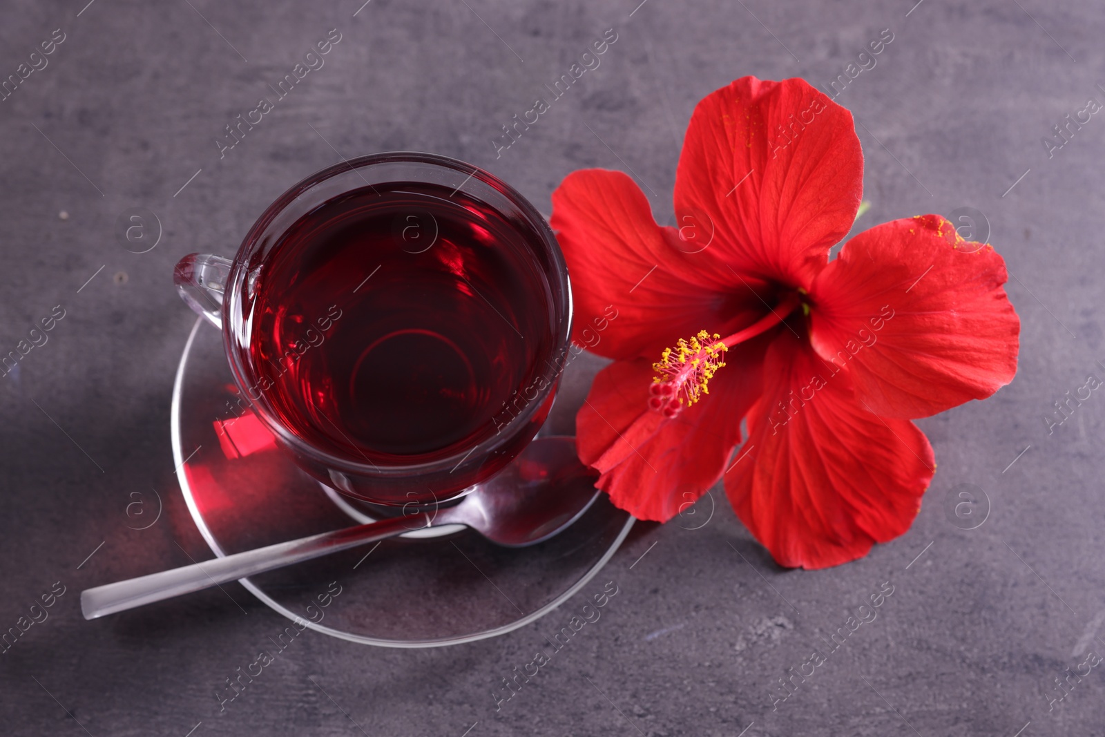 Tasty hibiscus tea in cup and beautiful flower on grey textured table, closeup Photo of Tasty hibiscus tea in cup and beautiful flower on grey textured table, closeup