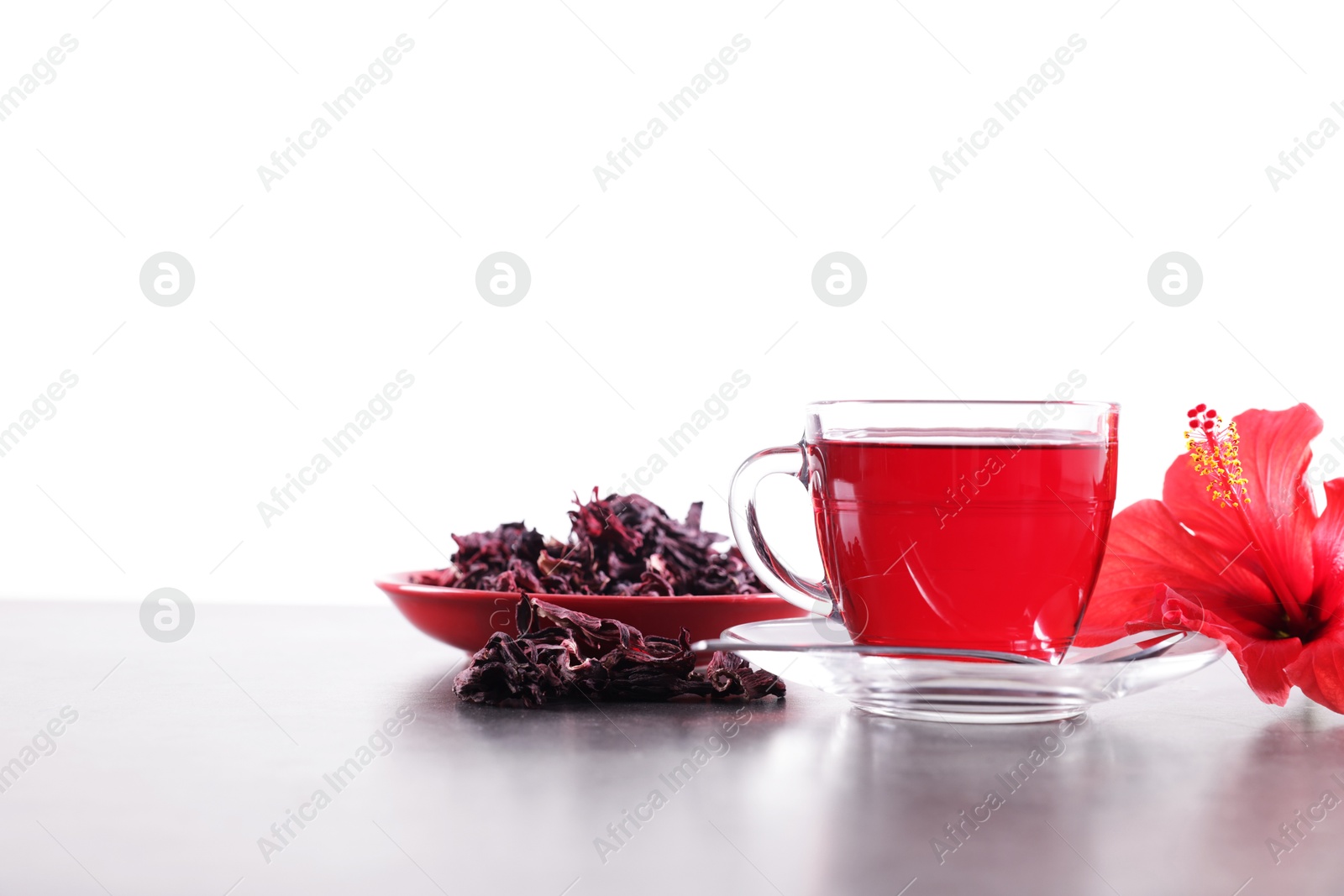 Tasty hibiscus tea in cup, dry roselle sepals and beautiful flower on grey textured table against white background. Space for text Photo of Tasty hibiscus tea in cup, dry roselle sepals and beautiful flower on grey textured table against white background. Space for text