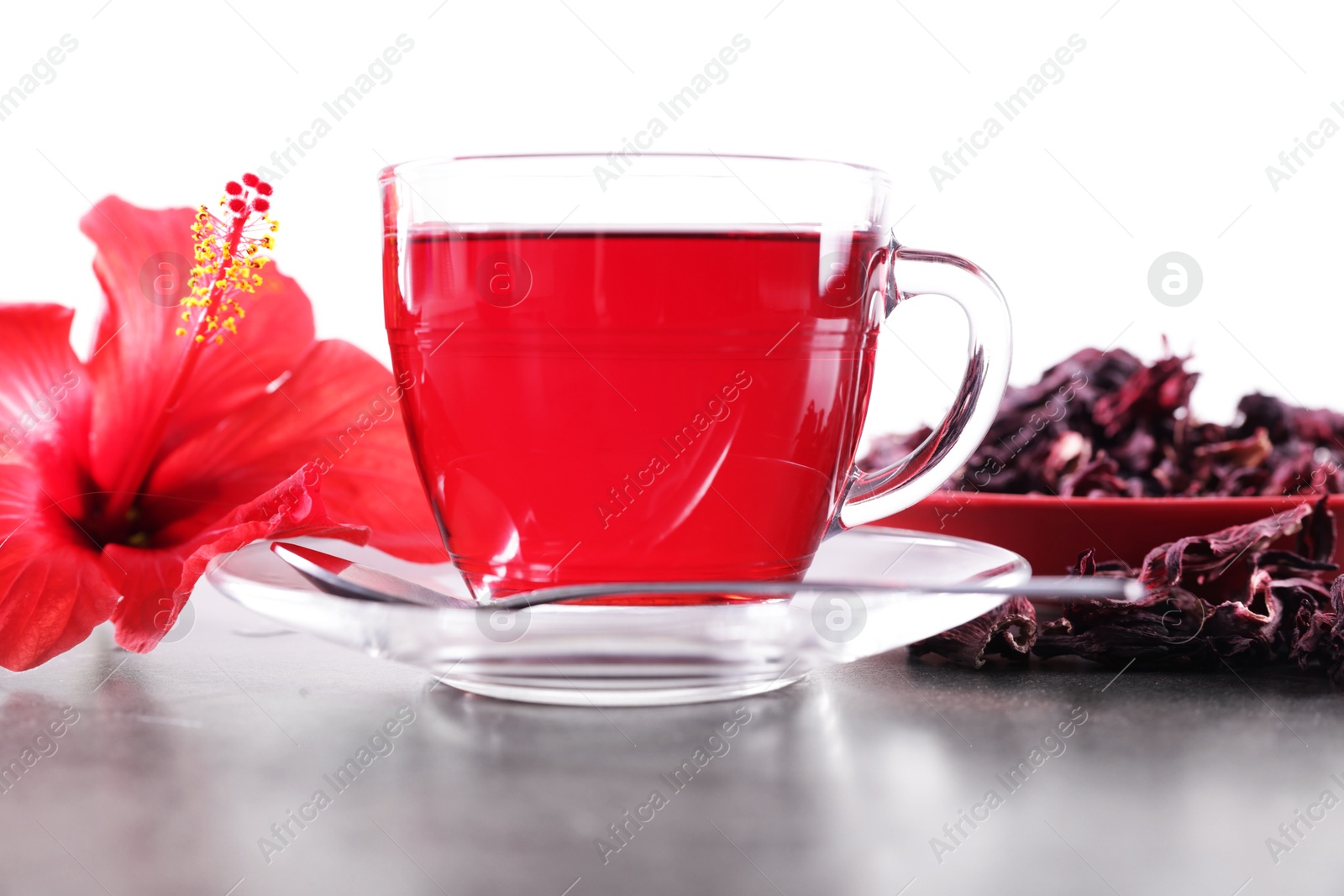 Tasty hibiscus tea in cup, dry roselle sepals and beautiful flower on grey textured table against white background Photo of Tasty hibiscus tea in cup, dry roselle sepals and beautiful flower on grey textured table against white background