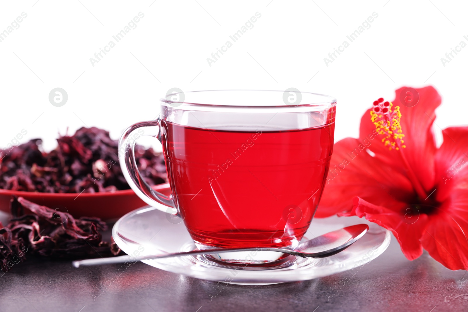 Tasty hibiscus tea in cup, dry roselle sepals and beautiful flower on grey textured table against white background Photo of Tasty hibiscus tea in cup, dry roselle sepals and beautiful flower on grey textured table against white background