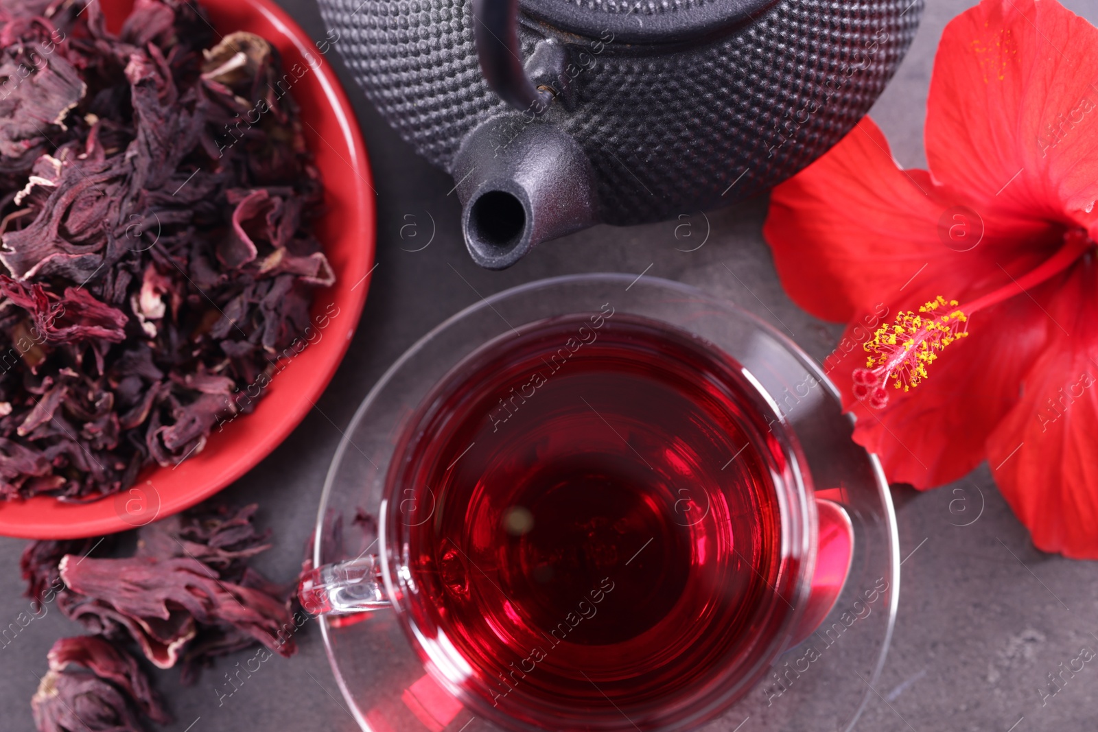Tasty hibiscus tea in cup, teapot, dry roselle sepals and beautiful flower on grey textured table, flat lay Photo of Tasty hibiscus tea in cup, teapot, dry roselle sepals and beautiful flower on grey textured table, flat lay