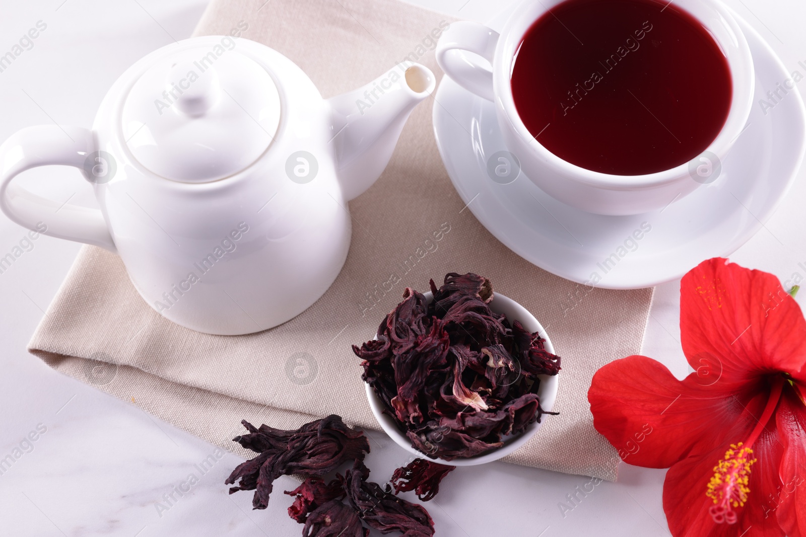 Tasty hibiscus tea, dry roselle sepals and beautiful flower on white table Photo of Tasty hibiscus tea, dry roselle sepals and beautiful flower on white table