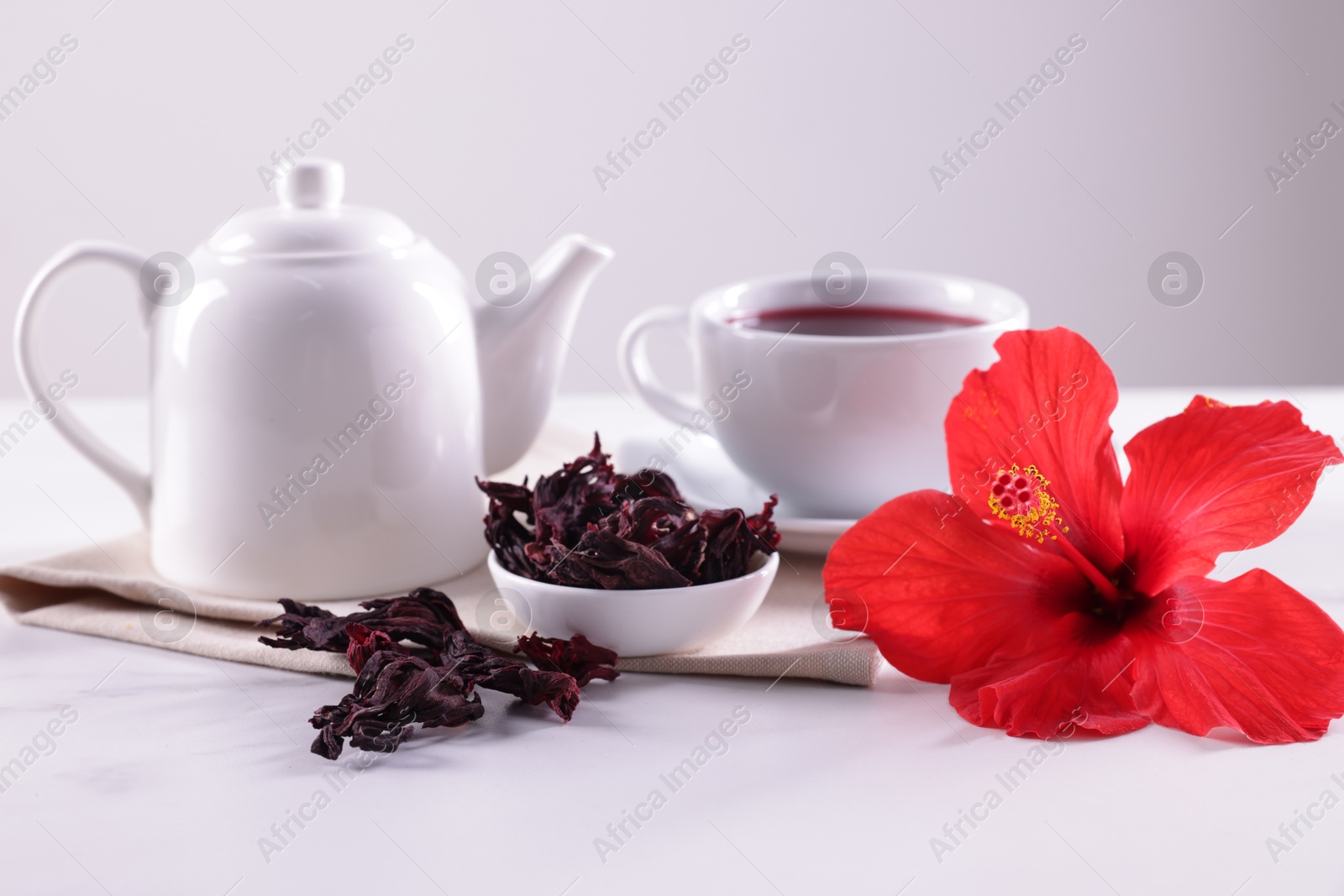 Tasty hibiscus tea, dry roselle sepals and beautiful flower on white table against grey background, closeup Photo of Tasty hibiscus tea, dry roselle sepals and beautiful flower on white table against grey background, closeup