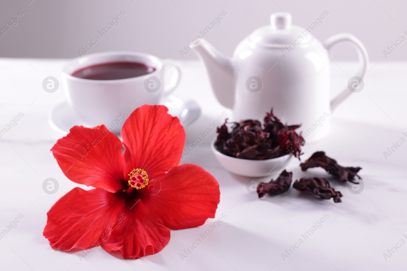Tasty hibiscus tea, dry roselle sepals and beautiful flower on white table against grey background, closeup Photo of Tasty hibiscus tea, dry roselle sepals and beautiful flower on white table against grey background, closeup