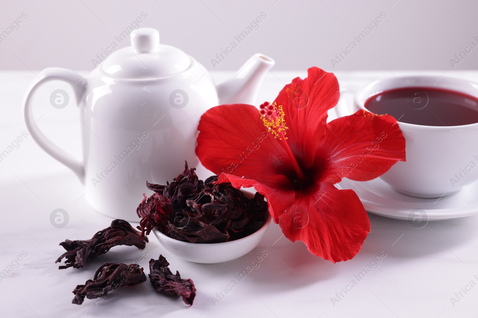 Tasty hibiscus tea, dry roselle sepals and beautiful flower on white table against grey background, closeup Photo of Tasty hibiscus tea, dry roselle sepals and beautiful flower on white table against grey background, closeup