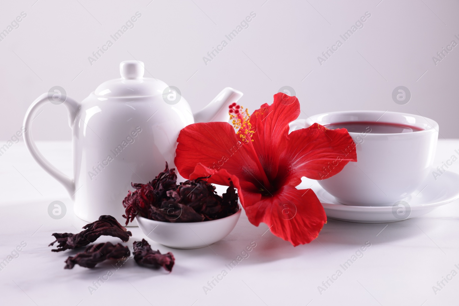 Tasty hibiscus tea, dry roselle sepals and beautiful flower on white table against grey background, closeup Photo of Tasty hibiscus tea, dry roselle sepals and beautiful flower on white table against grey background, closeup