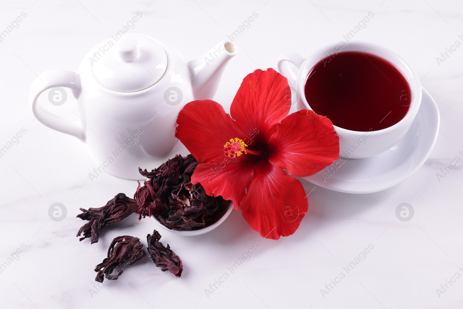 Tasty hibiscus tea, dry roselle sepals and beautiful flower on white table Photo of Tasty hibiscus tea, dry roselle sepals and beautiful flower on white table