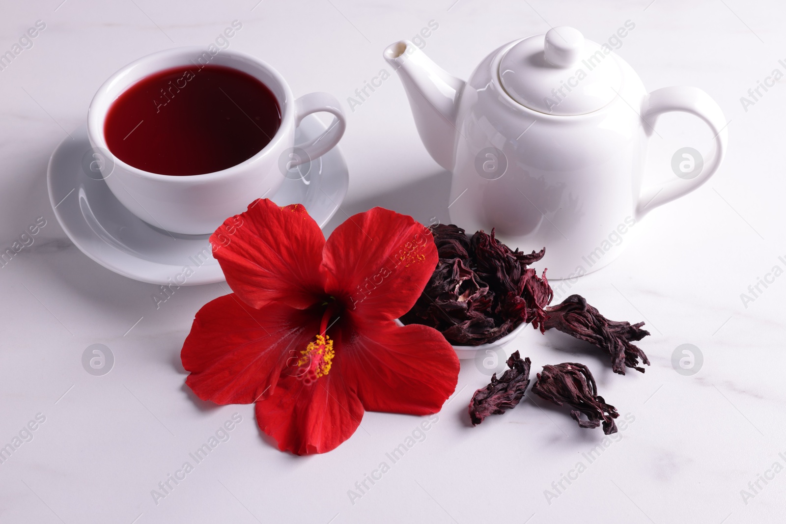 Tasty hibiscus tea, dry roselle sepals and beautiful flower on white table Photo of Tasty hibiscus tea, dry roselle sepals and beautiful flower on white table