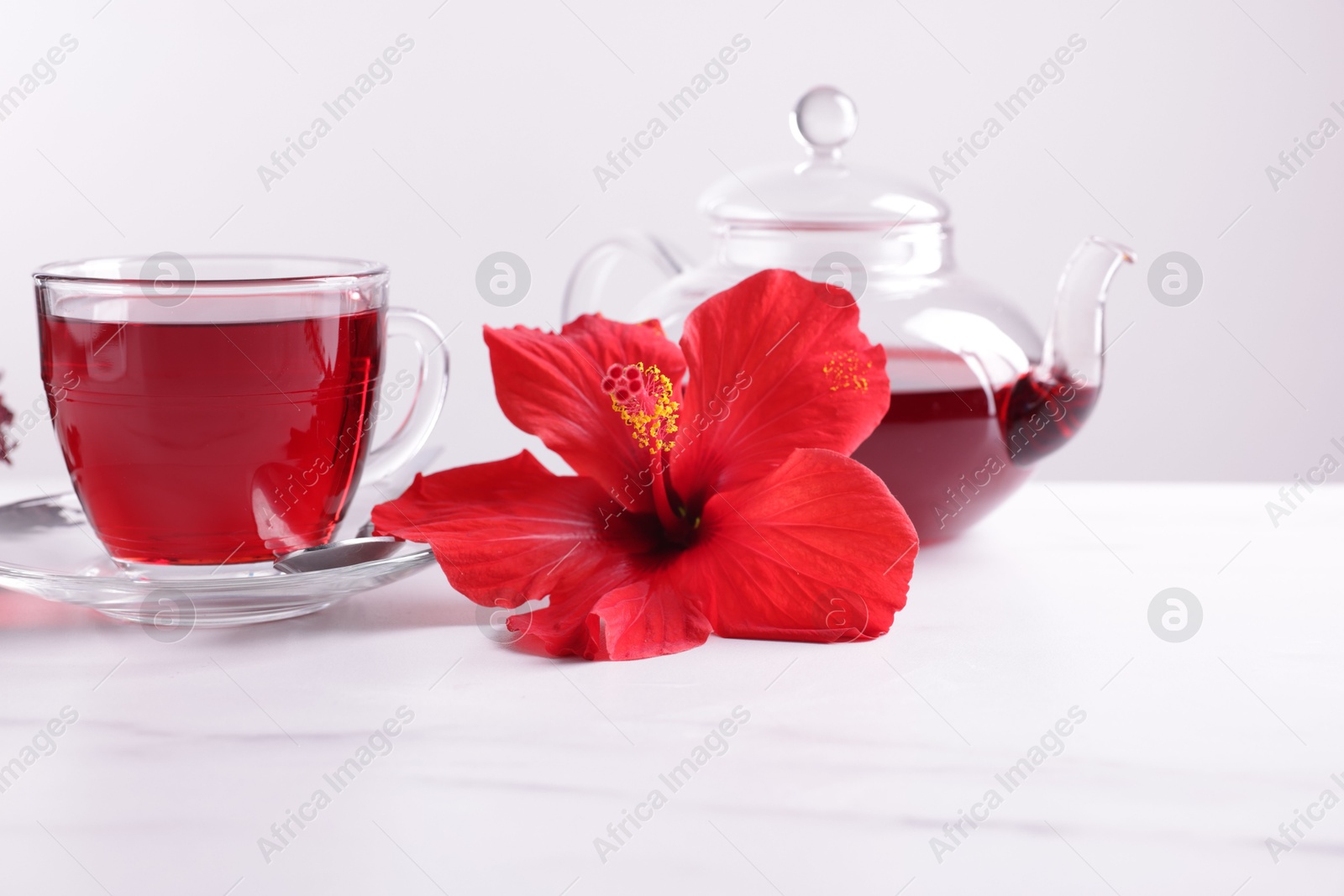 Tasty hibiscus tea and beautiful flower on white marble table against grey background, closeup Photo of Tasty hibiscus tea and beautiful flower on white marble table against grey background, closeup