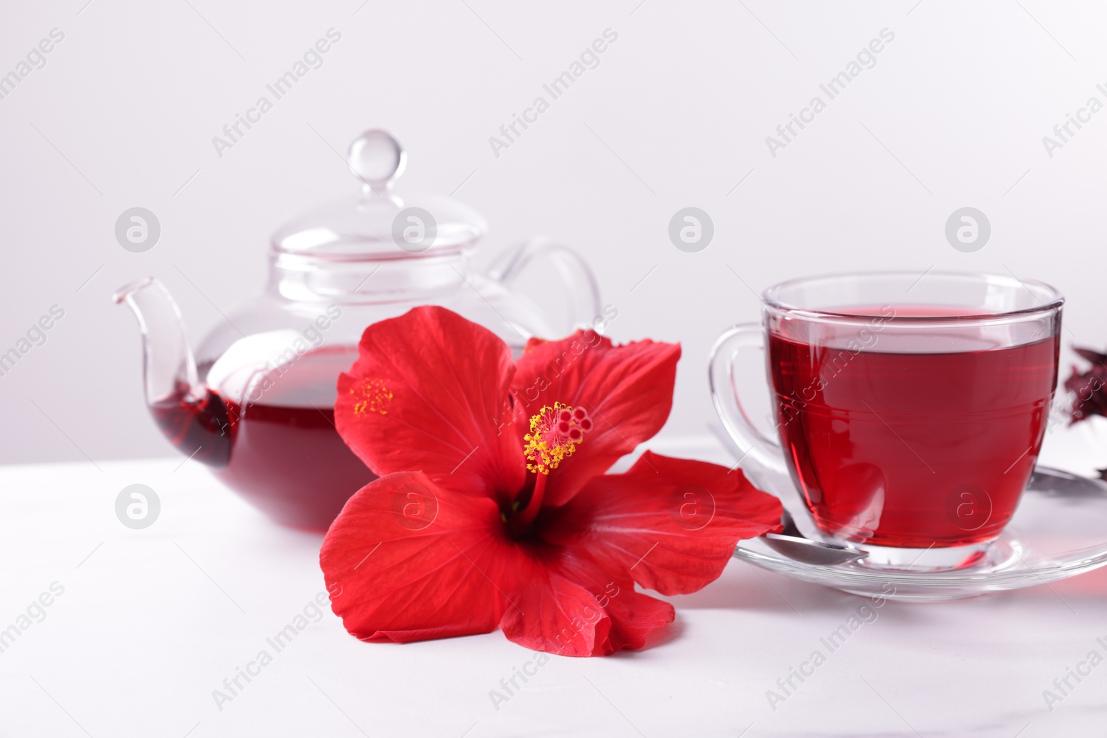 Tasty hibiscus tea and beautiful flower on white table against grey background, closeup Photo of Tasty hibiscus tea and beautiful flower on white table against grey background, closeup