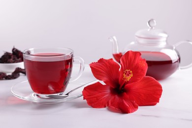 Photo of Tasty hibiscus tea, dry roselle sepals and beautiful flower on white marble table against grey background