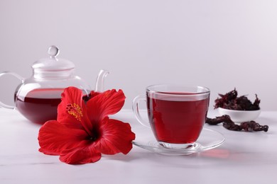 Photo of Tasty hibiscus tea, dry roselle sepals and beautiful flower on white marble table against grey background
