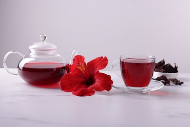 Photo of Tasty hibiscus tea, dry roselle sepals and beautiful flower on white marble table against grey background