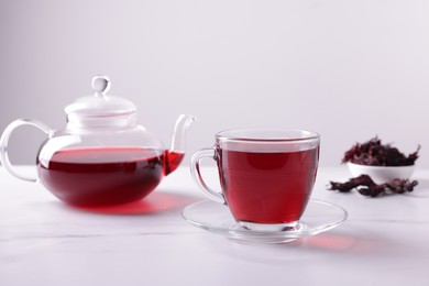 Photo of Tasty hibiscus tea, dry roselle sepals and beautiful flower on white marble table against grey background