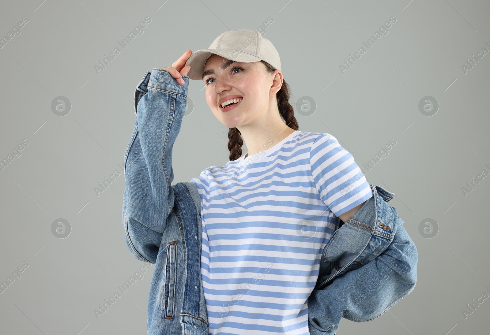 Happy woman in stylish baseball hat on grey background Photo of Happy woman in stylish baseball hat on grey background