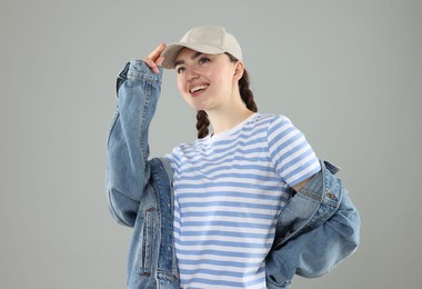 Photo of Happy woman in stylish baseball hat on grey background