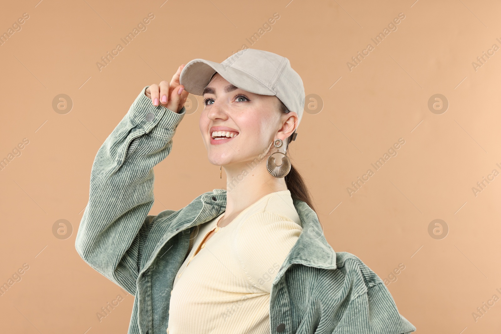Smiling woman in stylish baseball hat on beige background Photo of Smiling woman in stylish baseball hat on beige background