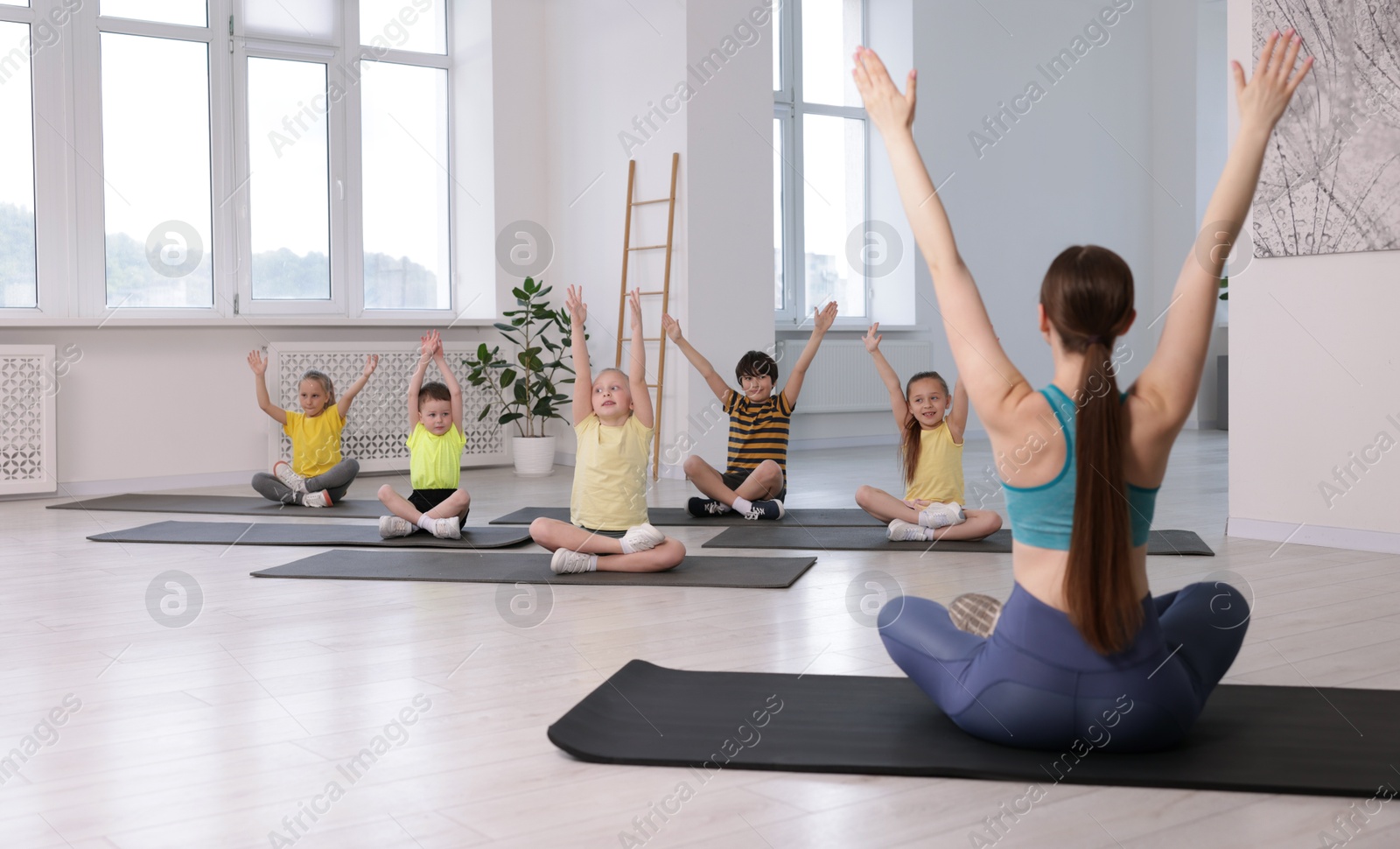 Group of children practicing yoga with coach on mats in class Photo of Group of children practicing yoga with coach on mats in class