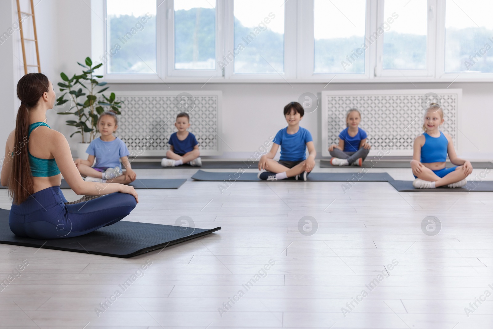 Group of children practicing yoga with coach on mats in class Photo of Group of children practicing yoga with coach on mats in class