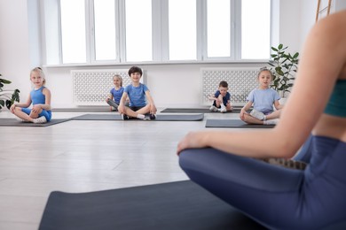 Photo of Group of children practicing yoga with coach on mats in class, selective focus