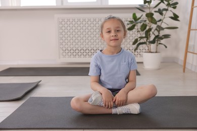 Photo of Cute girl sitting on yoga mat indoors