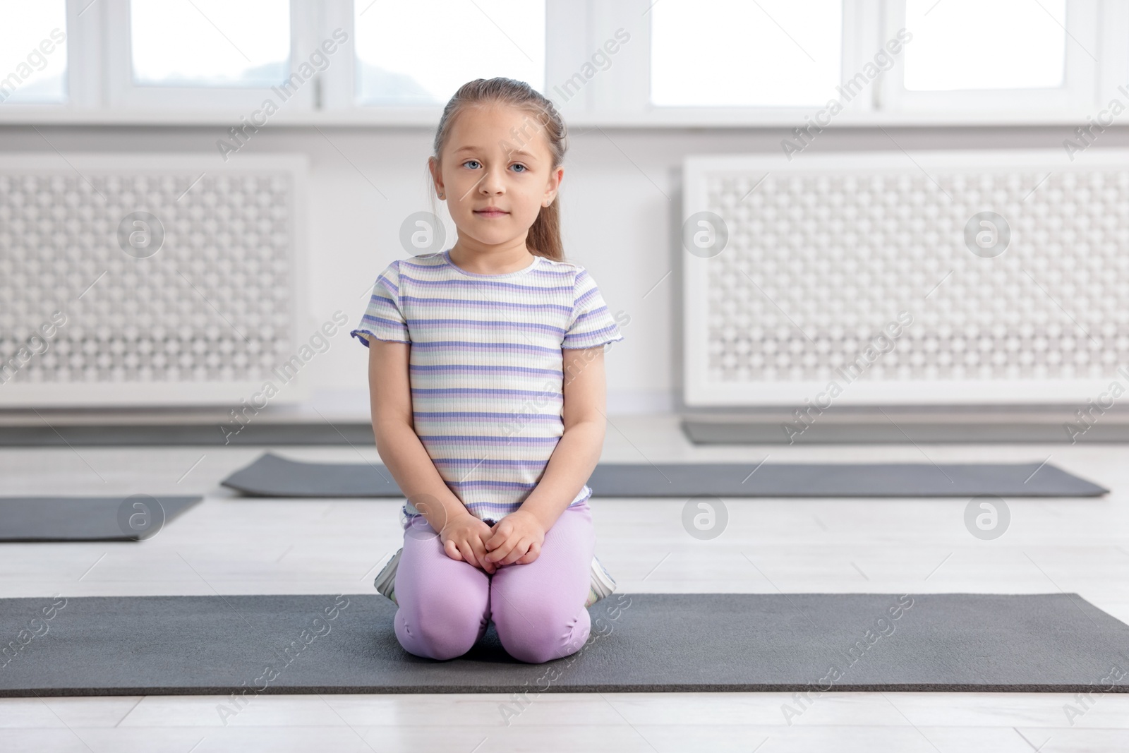 Cute girl sitting on yoga mat indoors Photo of Cute girl sitting on yoga mat indoors