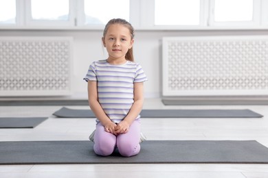 Photo of Cute girl sitting on yoga mat indoors