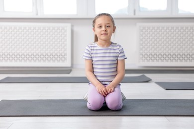 Photo of Cute girl sitting on yoga mat indoors