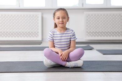 Photo of Cute girl sitting on yoga mat indoors