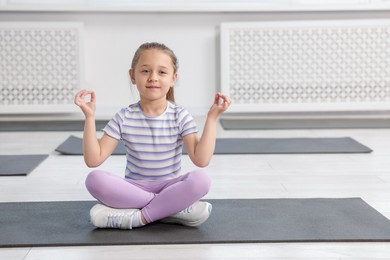Photo of Cute girl sitting on yoga mat indoors