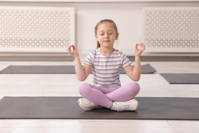 Photo of Cute girl meditating on yoga mat indoors