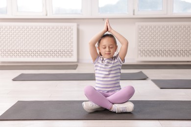 Photo of Cute girl meditating on yoga mat indoors