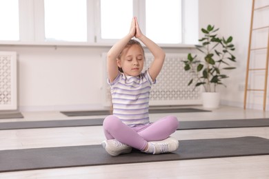 Photo of Cute girl meditating on yoga mat indoors