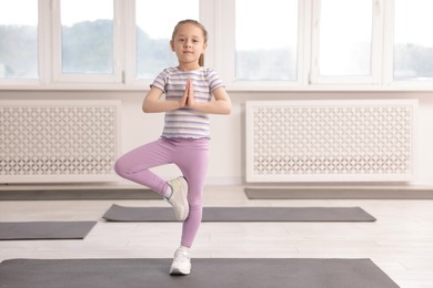 Photo of Cute girl practicing yoga on mat indoors