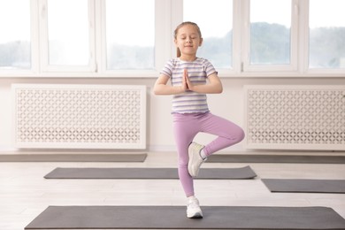 Photo of Cute girl practicing yoga on mat indoors