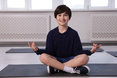 Photo of Happy boy practicing yoga on mat indoors
