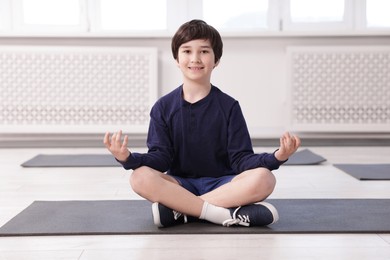 Photo of Happy boy practicing yoga on mat indoors