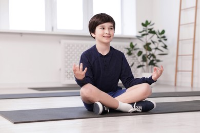 Photo of Happy boy practicing yoga on mat indoors