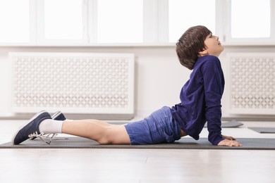 Photo of Cute boy practicing yoga on mat indoors