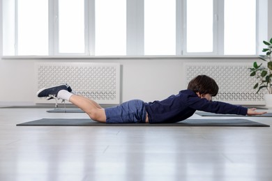 Photo of Cute boy practicing yoga on mat indoors