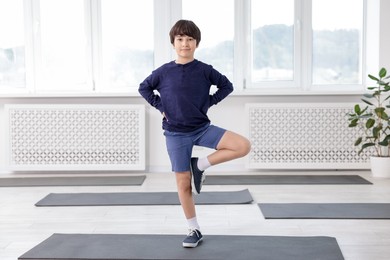 Photo of Cute boy practicing yoga on mat indoors