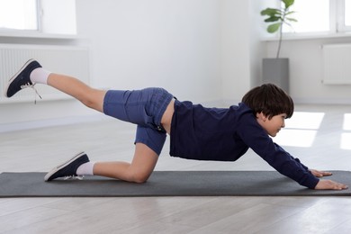 Photo of Cute boy practicing yoga on mat indoors