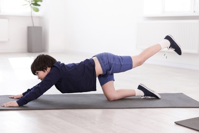 Photo of Cute boy practicing yoga on mat indoors