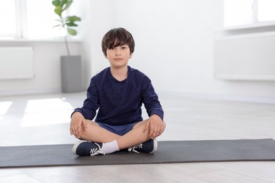 Photo of Cute boy sitting on yoga mat indoors