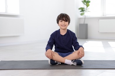 Photo of Happy boy sitting on yoga mat indoors