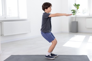 Photo of Cute boy exercising on yoga mat indoors